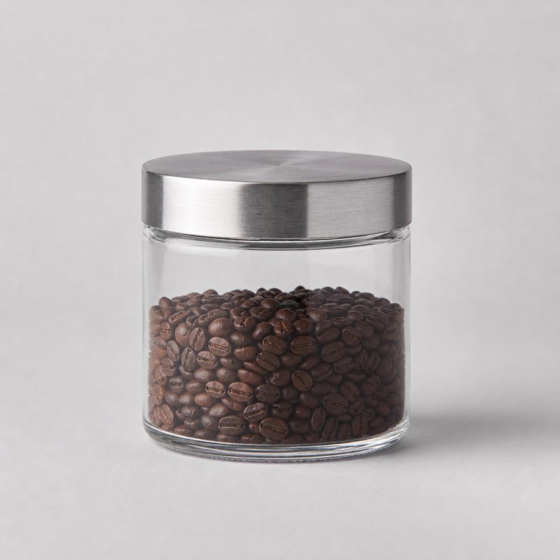 Small glass storage jar with a brushed steel lid, half filled with roasted beans