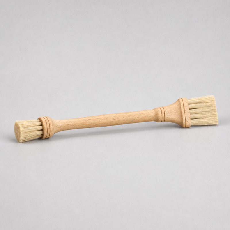 Double-ended wooden brush with pale stiff bristles at both ends lying flat