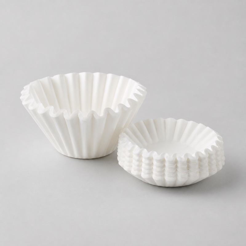 Folded white pleated paper coffee filter standing open beside a flat stack