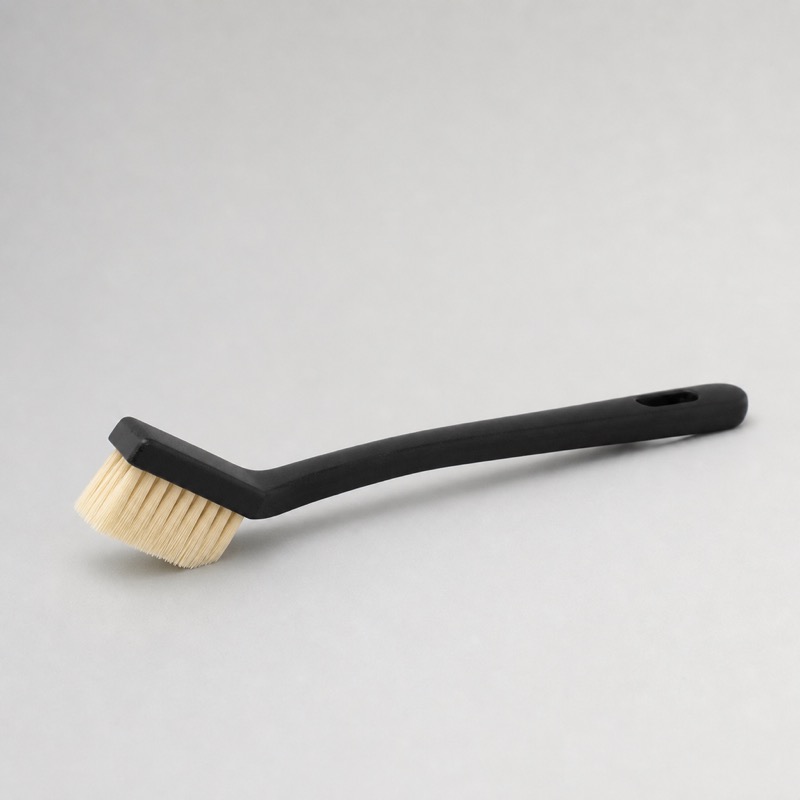 Cleaning brush with a black handle and an angled head of pale nylon bristles