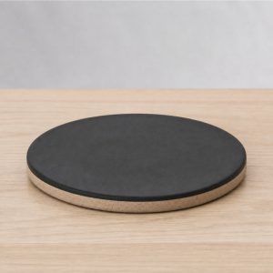 Round black ceramic trivet with an unglazed rim on a light wooden counter