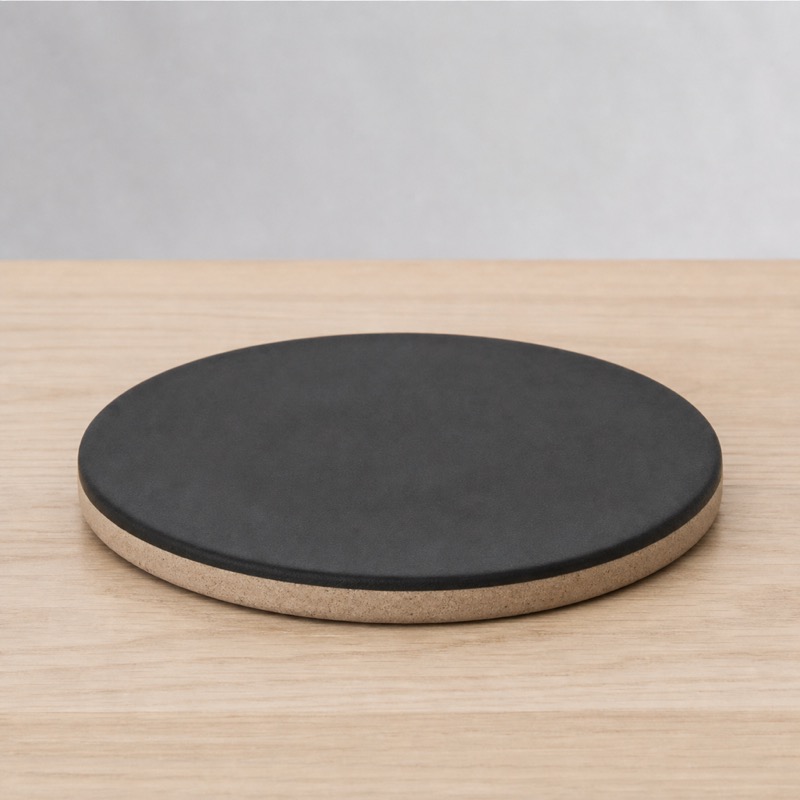 Round black ceramic trivet with an unglazed rim on a light wooden counter