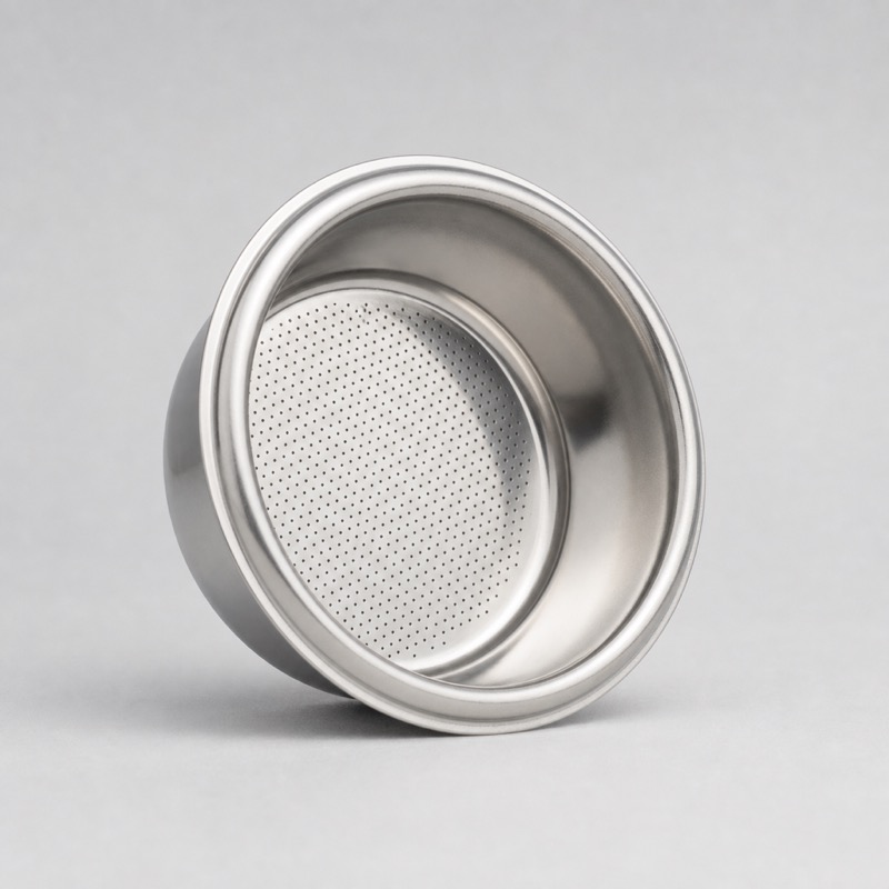 Stainless espresso filter basket standing on its side to show the drilled plate